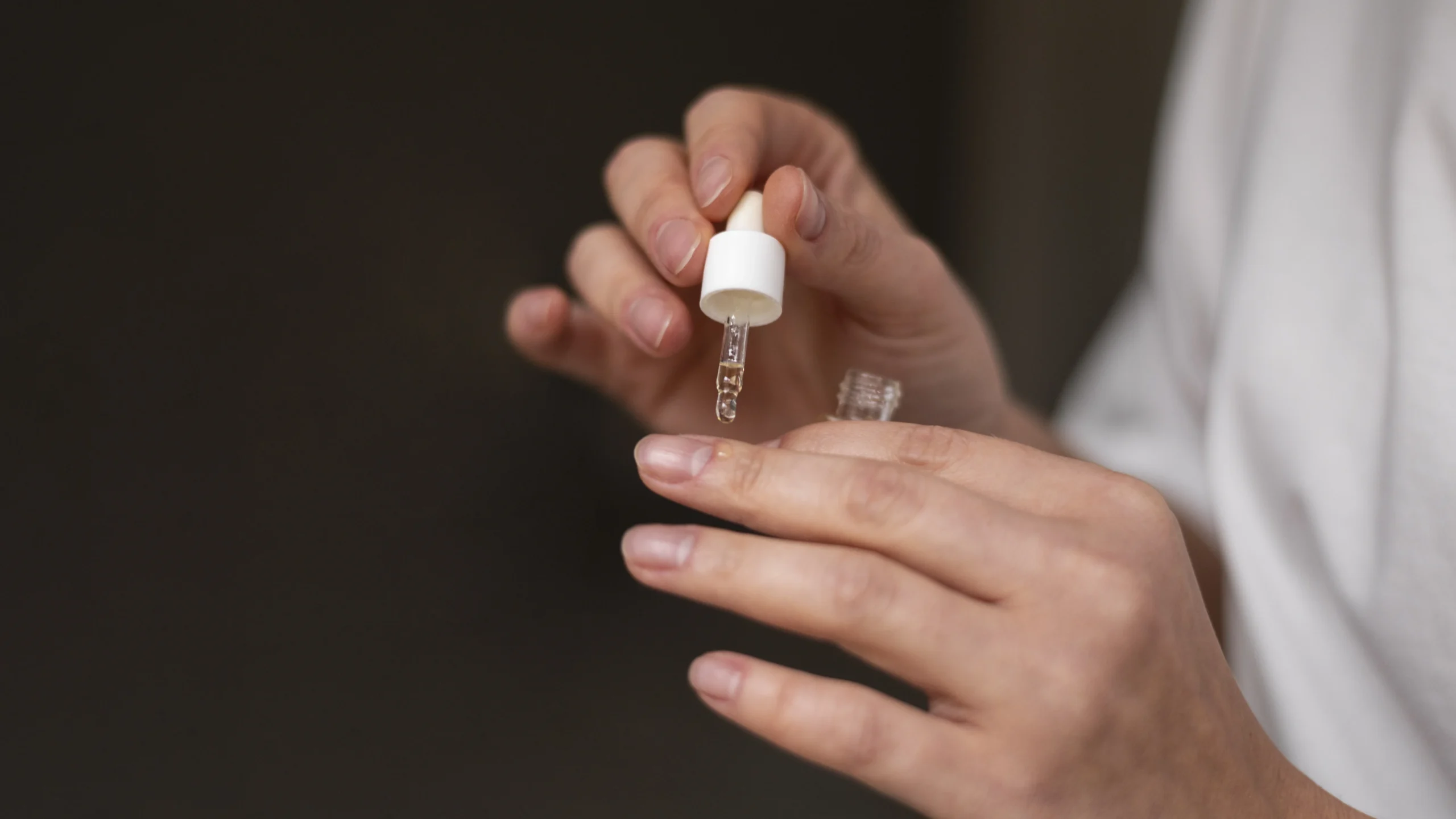 A close-up of a hand holding a dropper bottle filled with clear liquid, carefully applying it to another person's arm, demonstrating an essential step in maintaining healthy nails and understanding how long acrylic nails last.