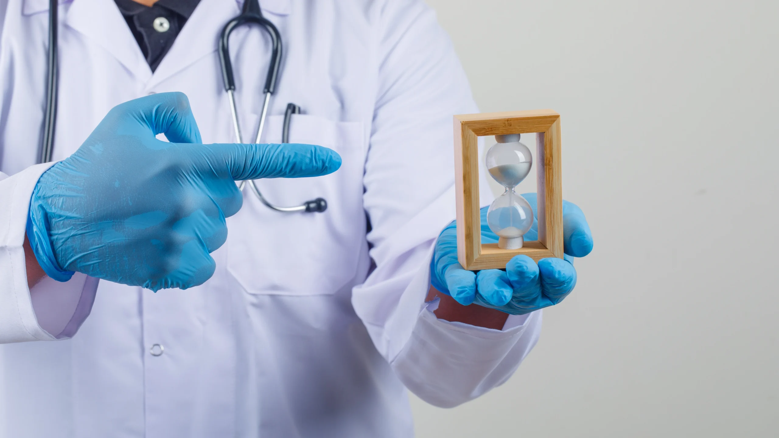 A healthcare professional wearing a lab coat and gloves holds an hourglass, symbolizing the passage of time and the topic of understanding the Maximum Delay in Periods if Not Pregnant