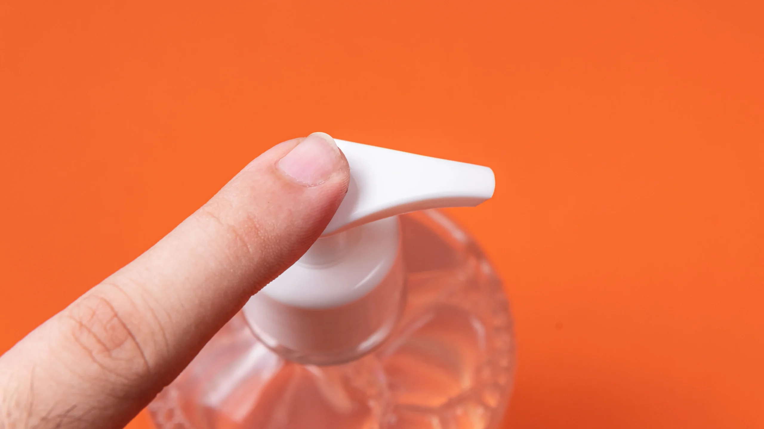 Close-up of a man's hand holding a container of alcohol gel on an orange background. Useful for hygiene, alcohol gel can also help remove nail polish from clothes in a pinch — part of effective solutions for 'How to Get Nail Polish Out of Clothes.