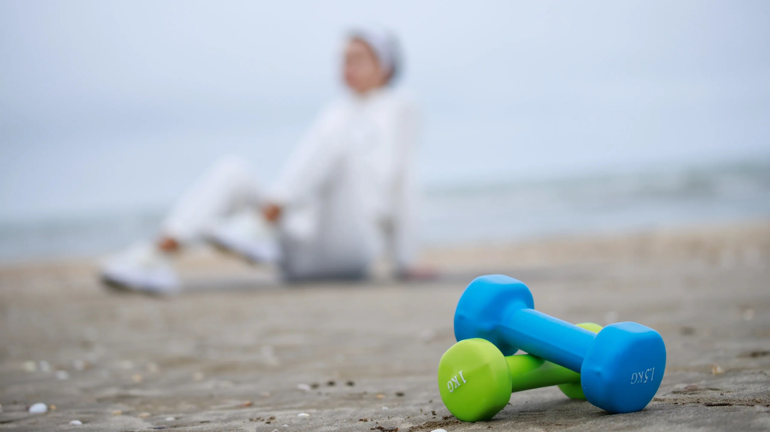 Colorful dumbbells resting on the sand at the beach, symbolizing exercise and physical activity, which can be a factor in delayed periods due to excessive exercising